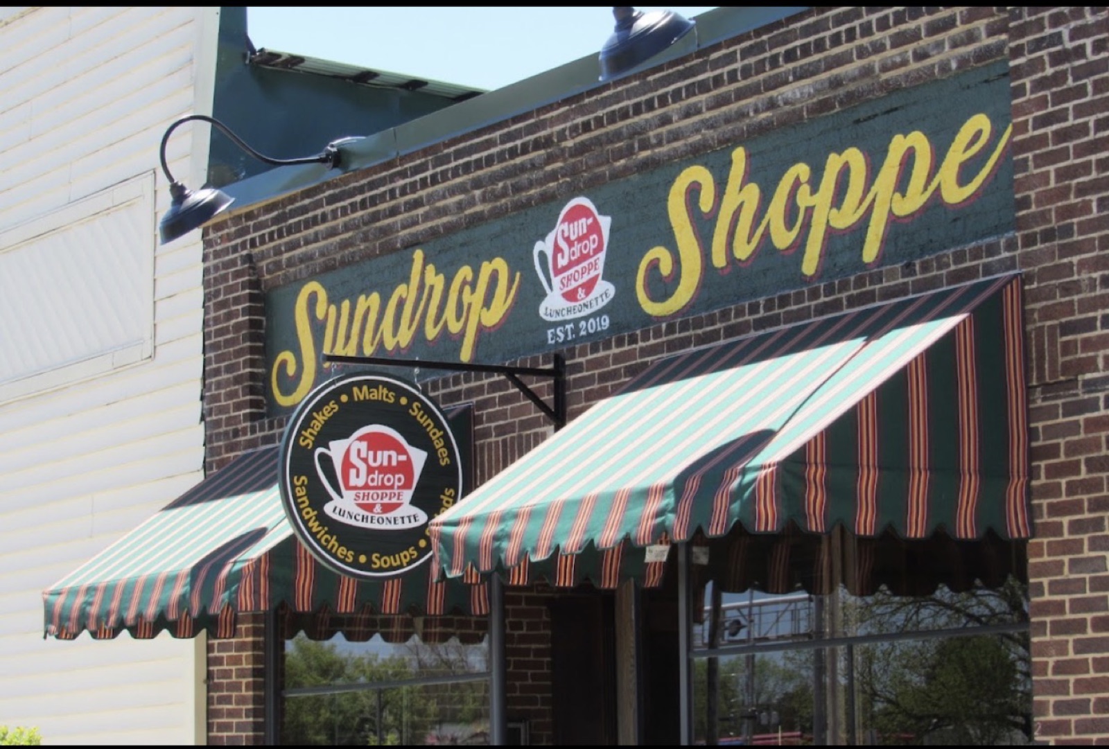 Hand-painted Sundrop Shoppe sign and striped awnings above the storefront windows